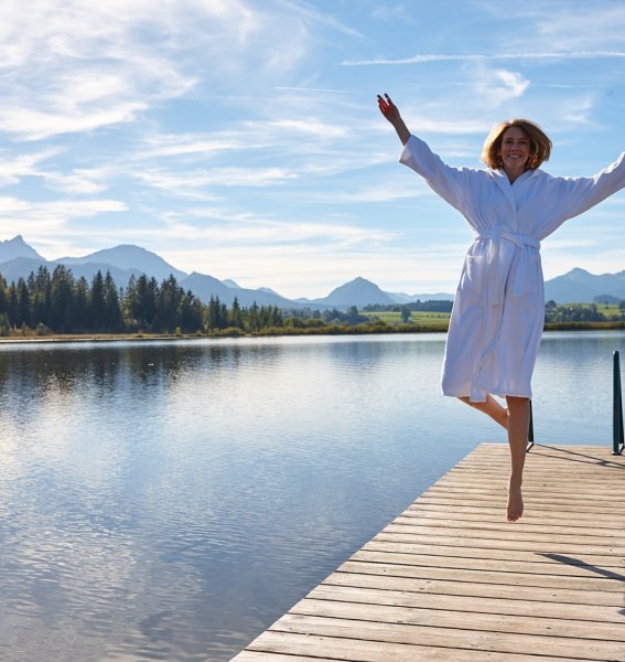 Eine Frau springt in die Luft auf einem Steg am See des Biohotel Eggensberger in Hopfen am See.