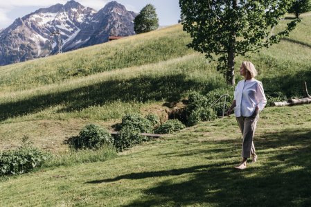 Eine Dame läuft entlang einer Wiese mit Bergpanorama beim Naturhotel Chesa Valisa.