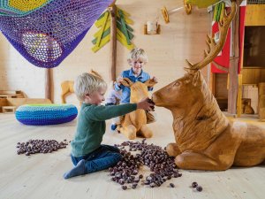 Zwei Kinder spielen mit einem hölzernen Hirsch und füttern ihn mit Kastanien im Indoorspielplatz des Familotel Allgäuer Berghof in Gunzesried.