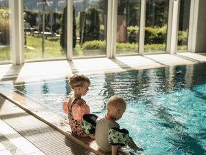 Zwei Kinder mit Schwimmflügeln sitzen am Beckenrand des Hallenbads des Mondi Resort in Oberstaufen.