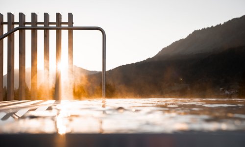 Der Sonnenuntergang spiegelt sich im Wasser des Außenpools des Genuss & Aktivhotel in Riezlern.