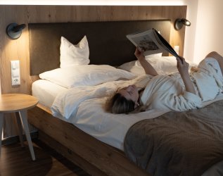 Eine Frau liest ein Magazin während sie auf dem Bett eines Zimmers des Kühberg in Oberstdorf liegt.