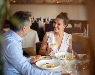 Ein Paar sitzt an einem gedeckten Tisch und trinkt Weißwein im Hotel Exquisit in Oberstdorf.