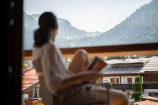 Eine Frau sitzt auf einem Balkon im Hotel Equisit in Oberstdorf und genießt die Aussicht.