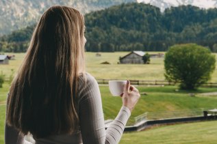Eine Frau genießt die Aussicht vom Balkon eines Zimmers des SCHÜLE´S Gesundheitsresort und Spa in Oberstdorf.