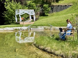 Inhaberin Sabine Gross arbeitet am Laptop auf einer Bank im Naturteich des Hotel Prinz-Luitpold-Bad in Bad Hindelang.