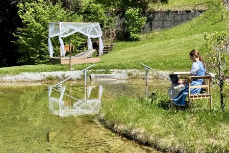 Hotel Prinz-Luitpold-Bad Teich Inhaberin Sabine Gross arbeitet am Laptop auf einer Bank im Naturteich des Hotel Prinz-Luitpold-Bad in Bad Hindelang.