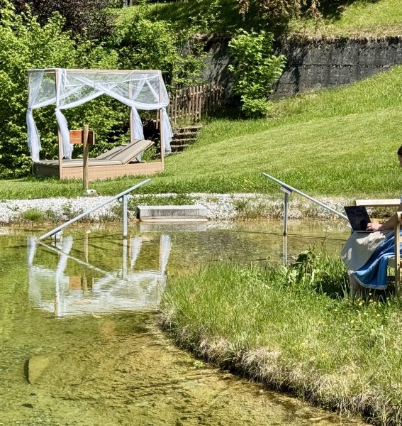 Inhaberin Sabine Gross arbeitet am Laptop auf einer Bank im Naturteich des Hotel Prinz-Luitpold-Bad in Bad Hindelang.