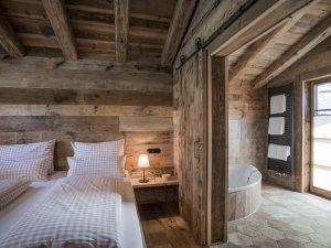 Blick auf das Doppelbett und Teil des Badezimmers mit Badewanne der Alpin Chalets in Oberjoch