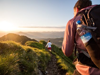 Allgäuer Alpenwasser Wandern Ein Mann mit einer Allgäuer Alpenwasser Flasche im Rucksack wandert hinter einer Frau