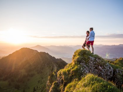 Allgäuer Alpenwasser Wandern Zwei Personen stehen auf einer Anhöhe beim Wandern und blicken in die Ferne