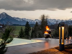 Blick auf den Relax Pool der Naturlodes im Sonnenalp Resort in Ofterschwang mit Blick auf verschneite Bergketten und Feuerschalen