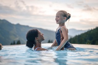 Eine Dame und ein Kind platschen im Außenpool im Oberjoch Familux Resort in Bad Hindelang.