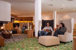 Personen genießen eine Auszeit in den Sesseln vor dem Kamin in der Lounge des Hotel Oberstdorf in Oberstdorf