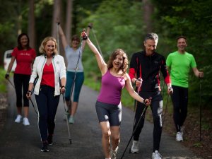 Eine Gruppe von Gästen unternimmt eine Nordic Walking Tour mit Dehnübungen durch einen Wald in der Nähe des Rosenalp Gesundheitsresorts und Spa in Oberstaufen