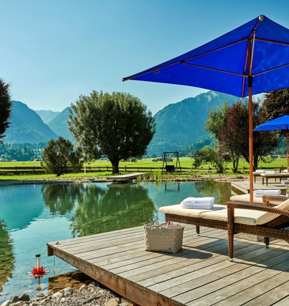 Eindruck vom Naturteich mit Liegen am Steg und Bergpanorama im Schüle's Gesundheitsresort und SPA in Oberstdorf im Sommer