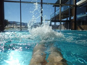 Ein Gast schwimmt im Innenpool mit großen bodenlangen Fenstern des Rosenalp Gesundheitsresorts und Spa in Oberstaufen