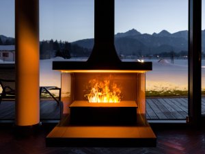 Ein Feuer im Kamin mit der schneebedeckten Umgebung im Hintergrund sorgt für eine schöne Stimmung an einem Winterabend im Hotel König Ludwig in Schwangau