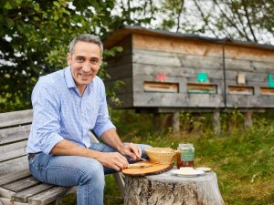 Der Hotelier vom Hanusel Hof in Weitnau / Hellengerst sitzt auf einer Bank im Garten und genießt frischen Honig