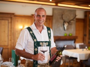 Hotelier Herr Reinalter mit einer Flasche Wein im Speiseraum des Hanusel Hofs in Weitnau