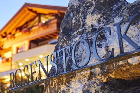 Hotellogo des Hotels Rosenstock in Fischen mit einem Teil des Hotelgebäudes im Hintergrund