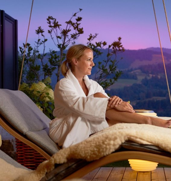 Eine Frau genießt den Sonnenuntergang auf einer der Schwebeliegen im Hotel Bergkristall - Mein Resort im Allgäu in Oberstaufen.