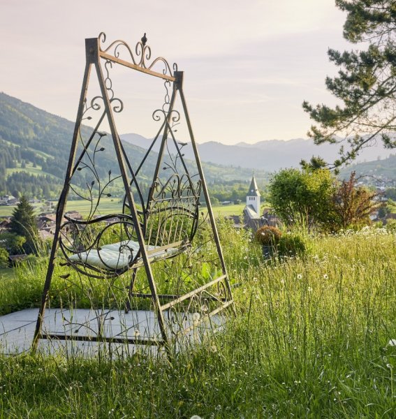 Außenbild des Hotel Prinz-Luitpold-Bads in Bad Hindelang mit Blick auf eine Eisenschaukel und der schönen Landschaft inklusive grünen Wiesen und Bergpanorama