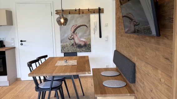 In der Küche stehen ein Tisch, Stühle und ein Fernseher an der Wand. Es gibt auch ein Bild mit einem Steinbock im Raum.