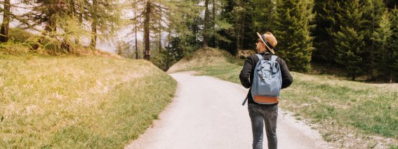 Mannlicher-reisender-mit-grossem-blauen-rucksack-der-zum-walddickicht-geht-und-sich-mit-interesse-umschaut