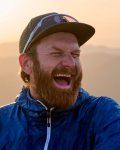 Ein Mann lacht während einer Wanderung in den Bergen. Die Sonne scheint und es ist Abend.