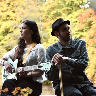 Nijala - Indie Pop Duo Ein Mann und eine Frau spielen Musik vor bunten Bäumen im Herbst. Sie genießen die Zeit im Freien und lächeln.