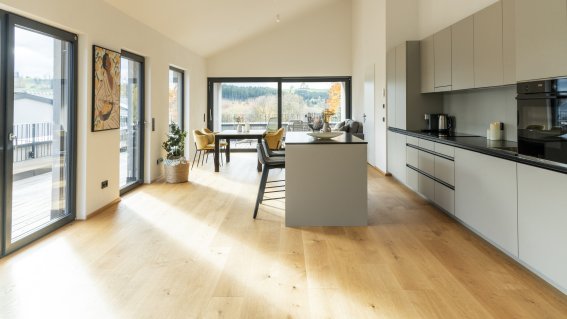 Der Raum zeigt eine großzügige Gestaltung mit Fenstern, einem Tisch und einer modernen Kücheneinheit.