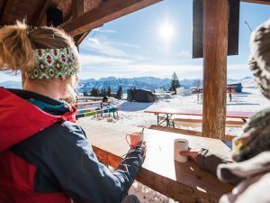 Eine Person genießt warme Getränke in den Bergen, während die Sonne über schneebedeckten Gipfeln scheint.