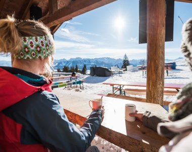 Eine Person genießt warme Getränke in den Bergen, während die Sonne über schneebedeckten Gipfeln scheint.
