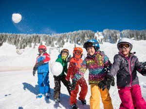 Fünf Kinder spielen im Schnee, werfen Schneebälle und genießen einen sonnigen Wintertag in den Bergen.