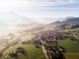 Die Sonne strahlt über ein malerisches Tal in den Alpen, während der Nebel das Land umhüllt. Ein ruhiger und friedlicher Morgen.