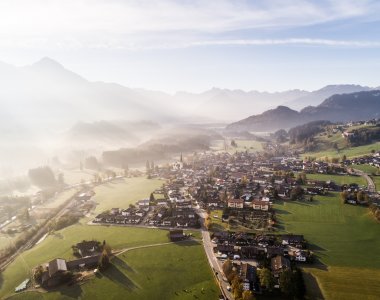 Die Sonne strahlt über ein malerisches Tal in den Alpen, während der Nebel das Land umhüllt. Ein ruhiger und friedlicher Morgen.