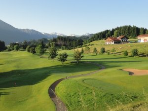 Golfspieler genießen unter blauem Himmel die malerische Landschaft mit Bergen und Wiesen während eines schönen Tages.