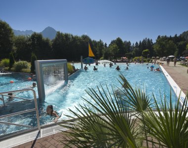 Viele Gäste entspannen und schwimmen in einem attraktiven Freizeitbad an einem sonnigen Sommertag.