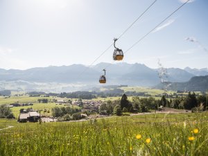 Die Seilbahn schwebt über weite Wiesen mit Bergblick an einem sonnigen Tag in den Alpen.