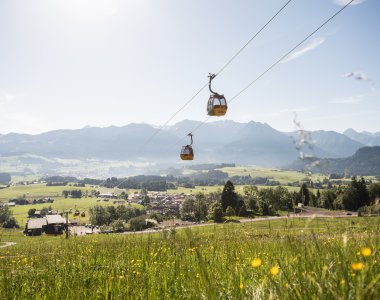 Die Seilbahn schwebt über weite Wiesen mit Bergblick an einem sonnigen Tag in den Alpen.