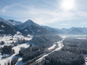 Schnee bedeckt die Berge und Täler in einer ruhigen Winterlandschaft unter einem hellen blauen Himmel.