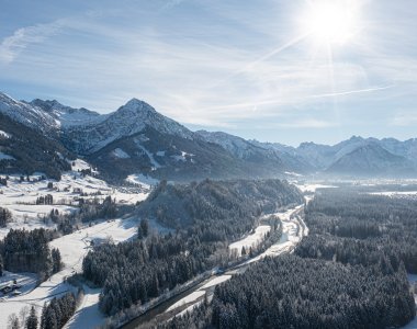 Schnee bedeckt die Berge und Täler in einer ruhigen Winterlandschaft unter einem hellen blauen Himmel.