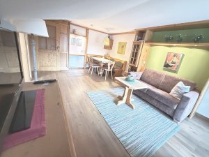 In dieser Wohnung sieht man ein Wohnzimmer mit einem Sofa, einem Tisch und Stühlen. Es gibt viel Holz und ein warmes Licht.