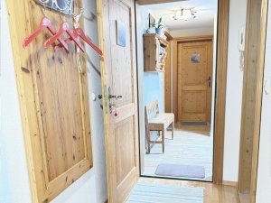 Der Flur zeigt eine Holzverkleidung mit einem Haken, einer Bank und zwei Türen. Es ist hell im Raum und freundlich.