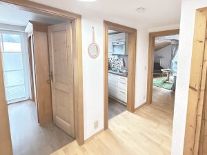 Der Flur führt zur Küche und zum Wohnzimmer in einer Wohnung. Es gibt Holzdetails und viel Licht.