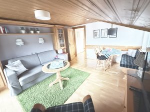 Ein gemütliches Wohnzimmer zeigt ein Sofa, einen Tisch und Stühle. Ein grüner Teppich liegt auf dem Boden.