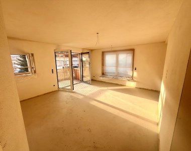 Der Raum in der Wohnung hat noch keine Möbel. Sonnenlicht fällt durch die Fenster.