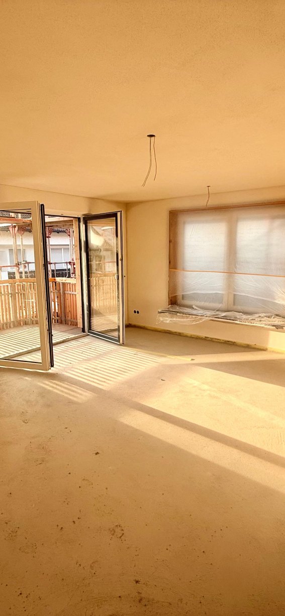 Der Raum in der Wohnung hat noch keine Möbel. Sonnenlicht fällt durch die Fenster.