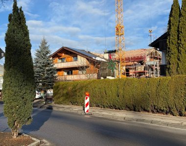 In einer Wohngegend sind Bauarbeiten an einem neuen Gebäude. Eine Baustelle ist sichtbar, Bäume sind in der Nähe.